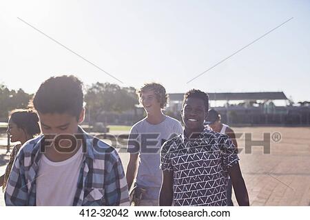 Stock Image - Smiling teenage friends at sunny skate park. Fotosearch