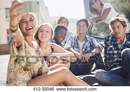 Smiling teenage friends posing for selfie on sunny urban street View Large Photo Image Stock Photograph - Smiling teenage friends posing for selfie on sunny urban street. Fotosearch