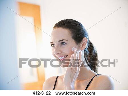 Stock Image - Smiling woman applying face cream to cheek. Fotosearch
