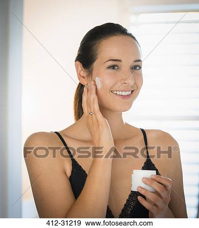 Smiling woman applying face cream to cheek in bathroom mirror View Large Photo Image Stock Photo - Smiling woman applying face cream to cheek in bathroom mirror. Fotosearch