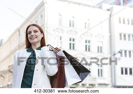 Stock Image - Smiling woman carrying shopping bags in city. Fotosearch
