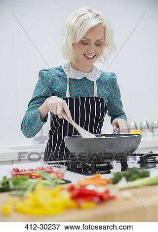 Stock Photo - Smiling woman in apron cooking in kitchen. Fotosearch