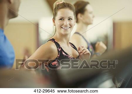 Stock Photography - Smiling woman jogging on treadmill at gym. Fotosearch