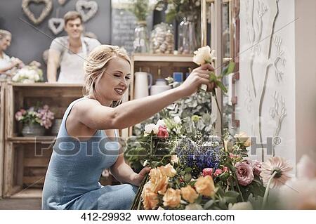 Stock Image - Smiling woman picking out flowers in flower shop. Fotosearch