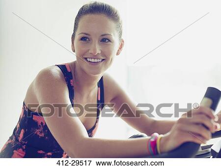 Smiling woman riding exercise bike at gym View Large Photo Image Stock Photo - Smiling woman riding exercise bike at gym. Fotosearch