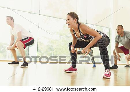 Stock Image - Smiling woman squatting in aerobics class. Fotosearch