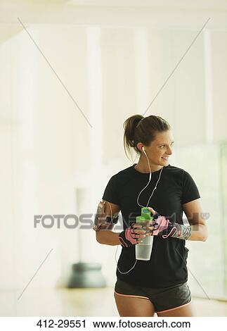 Stock Image - Smiling woman taking a break drinking water in gym studio. Fotosearch