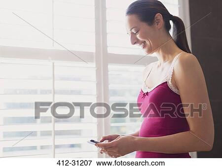 Stock Photo - Smiling woman texting with cell phone at window. Fotosearch