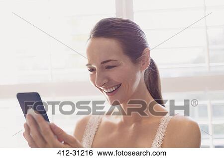 Smiling woman texting with cell phone at window View Large Photo Image Stock Photograph - Smiling woman texting with cell phone at window. Fotosearch