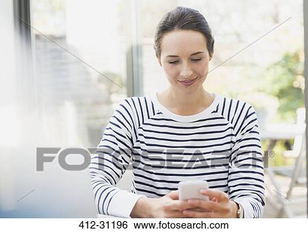Stock Photograph - Smiling woman using cell phone at sidewalk cafe. Fotosearch