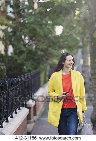 Smiling woman walking with cell phone in urban park View Large Photo Image Stock Photograph - Smiling woman walking with cell phone in urban park. Fotosearch