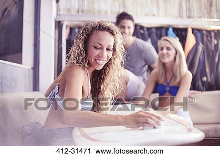 Stock Image - Smiling woman waxing surfboard. Fotosearch