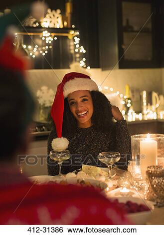 Stock Photograph - Smiling woman wearing Santa hat at candlelight Christmas dinner party. Fotosearch
