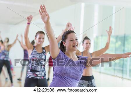 Stock Photograph - Smiling woman with arms raised in exercise class. Fotosearch
