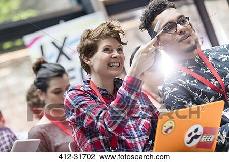 Stock Image - Smiling woman with laptop pointing at technology conference. Fotosearch