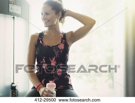 Smiling woman with water bottle resting at gym View Large Photo Image Stock Image - Smiling woman with water bottle resting at gym. Fotosearch