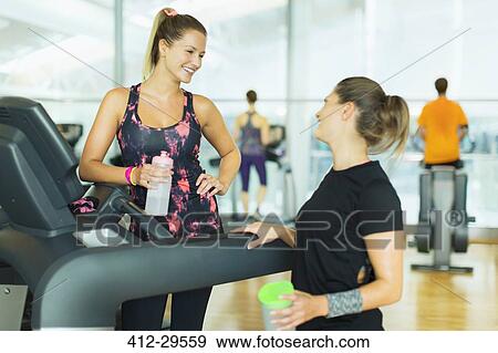 Stock Photo - Smiling women resting and talking at treadmill in gym. Fotosearch