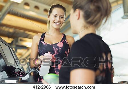 Smiling women talking and drinking water at gym View Large Photo Image Stock Image - Smiling women talking and drinking water at gym. Fotosearch