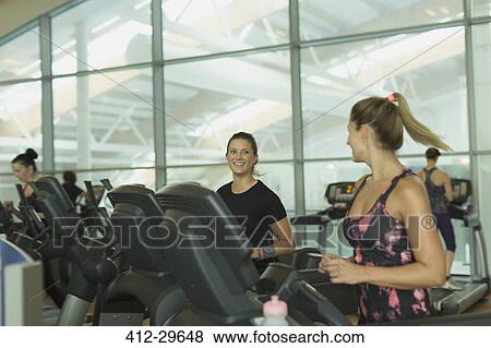 Smiling women talking and jogging on treadmills at gym View Large Photo Image Stock Photo - Smiling women talking and jogging on treadmills at gym. Fotosearch