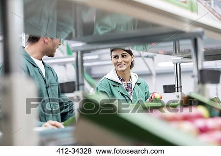 Stock Photo - Smiling workers processing apples in food processing plant. Fotosearch