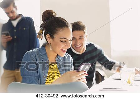 Smiling young business people texting with cell phone View Large Photo Image Stock Image - Smiling young business people texting with cell phone. Fotosearch