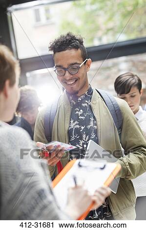 Stock Image - Smiling young man showing credentials at technology conference. Fotosearch