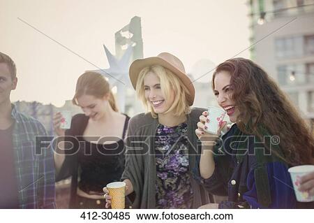 Smiling young women drinking and laughing at rooftop party View Large Photo Image Stock Photography - Smiling young women drinking and laughing at rooftop party. Fotosearch