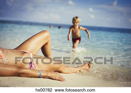 Son running toward mother sunbathing on sunny tropical beach View Large Photo Image Stock Image - Son running toward mother sunbathing on sunny tropical beach. Fotosearch