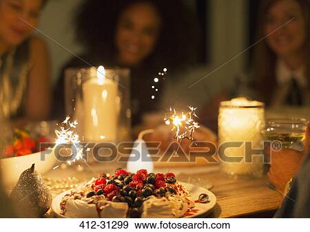 Stock Photo - Sparklers on berry pavlova dessert on candlelight table. Fotosearch