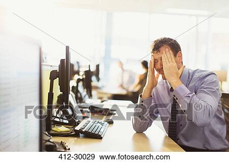 Stock Photo - Stressed businessman with head in hands at office desk. Fotosearch