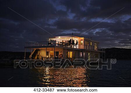 Stock Photo - Summer houseboat illuminated on night ocean. Fotosearch