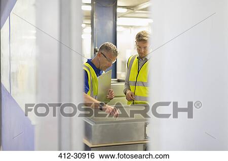 Stock Photograph - Supervisor and worker inspecting pieces in steel factory. Fotosearch