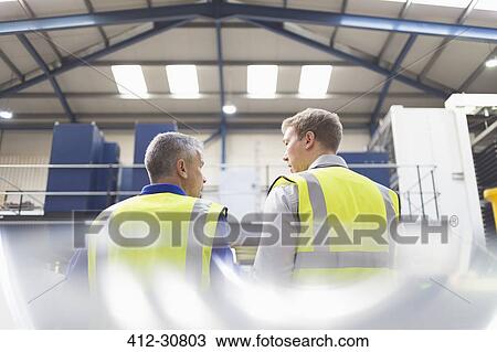 Stock Image - Supervisor and worker talking in steel factory. Fotosearch