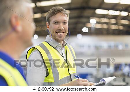 Supervisor with clipboard smiling at worker in steel factory View Large Photo Image Stock Image - Supervisor with clipboard smiling at worker in steel factory. Fotosearch