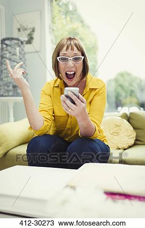 Stock Image - Surprised mature woman looking at cell phone receiving good news. Fotosearch