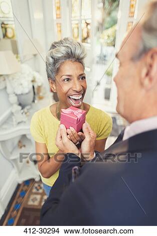 Picture - Surprised mature woman receiving gift from husband. Fotosearch