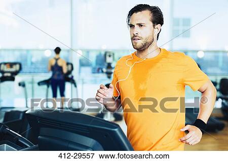 Stock Photo - Sweating man with headphones running on treadmill at gym. Fotosearch