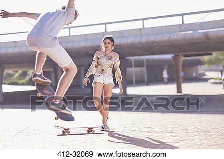 Stock Photo - Teenage boy and girl skateboarding at sunny skate park. Fotosearch