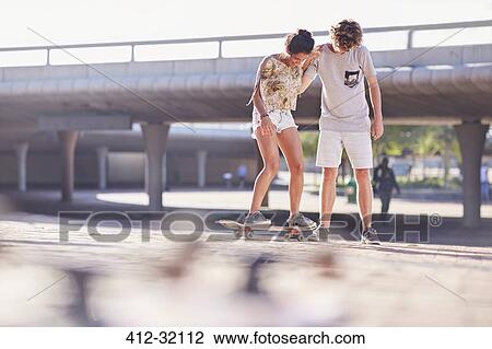 Teenage boy teaching girlfriend skateboarding at sunny skate park View Large Photo Image Stock Image - Teenage boy teaching girlfriend skateboarding at sunny skate park. Fotosearch