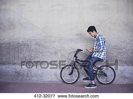 Stock Photo - Teenage boy texting on BMX bicycle at wall. Fotosearch