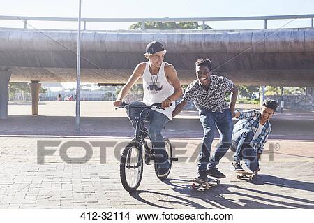Picture - Teenage boys riding BMX bicycle and skateboarding at sunny skate park. Fotosearch