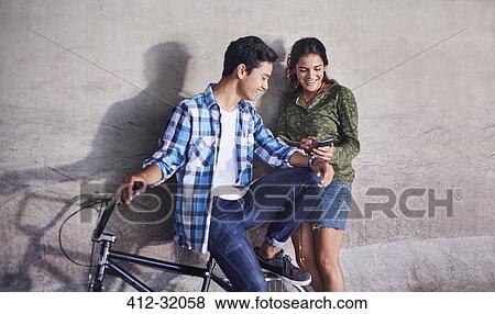 Teenage couple with BMX bicycle texting with cell phone at wall View Large Photo Image Stock Photo - Teenage couple with BMX bicycle texting with cell phone at wall. Fotosearch