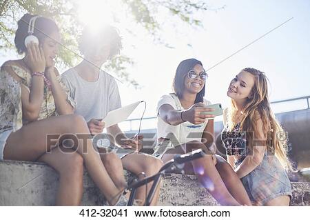 Stock Image - Teenage friends hanging out taking selfie and listening to music. Fotosearch