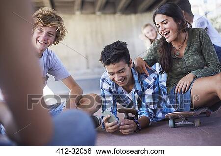 Teenage friends hanging out texting with cell phone at skate park View Large Photo Image Stock Photograph - Teenage friends hanging out texting with cell phone at skate park. Fotosearch
