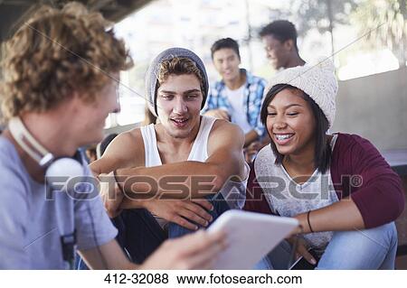 Teenage friends hanging out using digital tablet View Large Photo Image Stock Photo - Teenage friends hanging out using digital tablet. Fotosearch