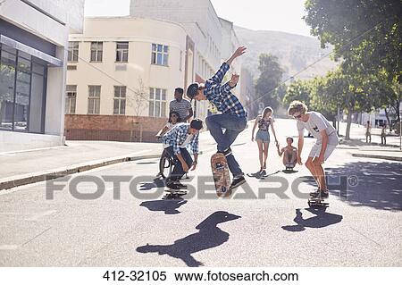 Teenage friends skateboarding on sunny urban street View Large Photo Image Stock Photography - Teenage friends skateboarding on sunny urban street. Fotosearch