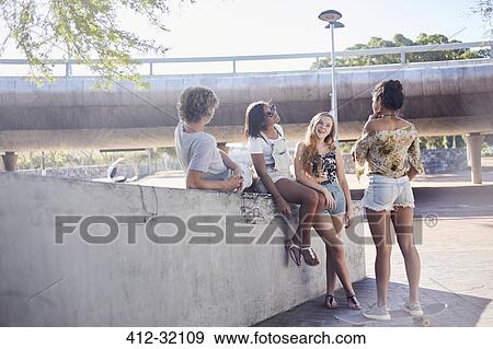Stock Photo - Teenage friends talking hanging out at sunny skate park. Fotosearch