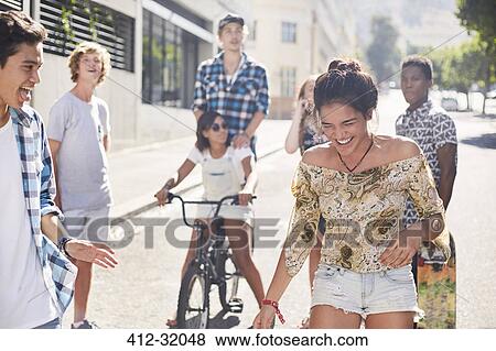 Stock Photo - Teenage girl laughing with friends on sunny urban street. Fotosearch