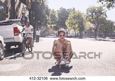 Teenage girl sitting riding skateboard on sunny urban street View Large Photo Image Stock Photograph - Teenage girl sitting riding skateboard on sunny urban street. Fotosearch