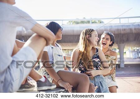 Stock Image - Teenage girls laughing hanging out at sunny skate park. Fotosearch